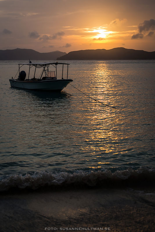 Båt i solnedgången och vågor mot strand.