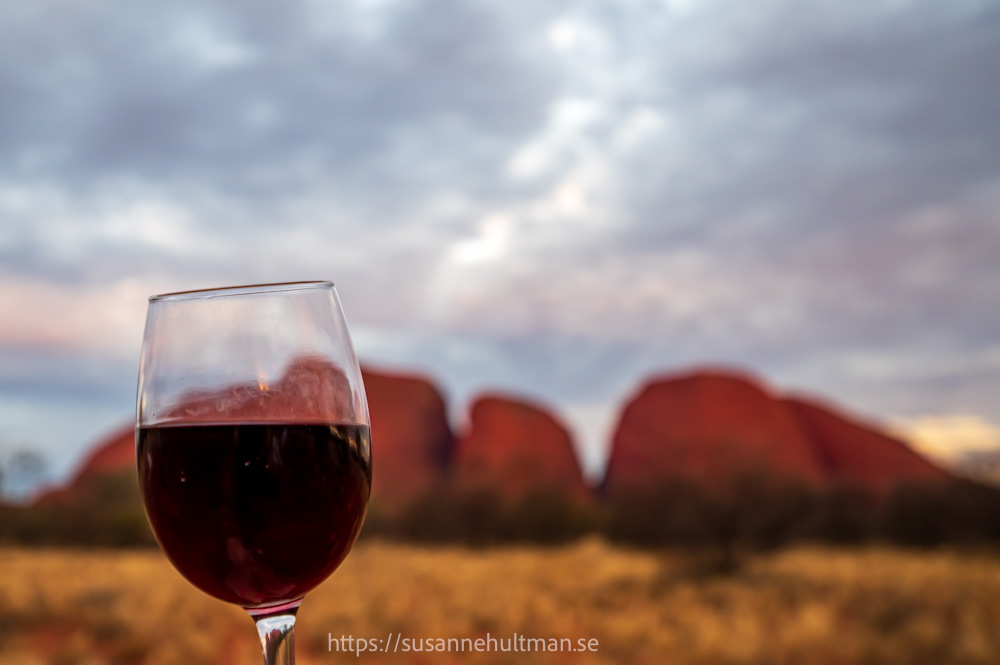 Ett glas rött vin framför Kata Tjuta i bakgrunden.